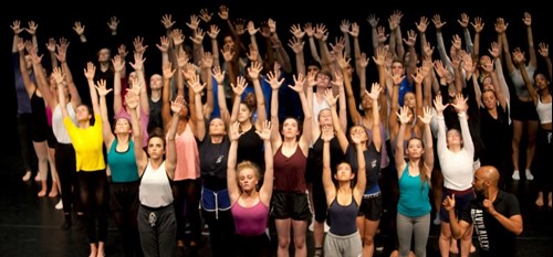 A large group of dancers with their arms raised